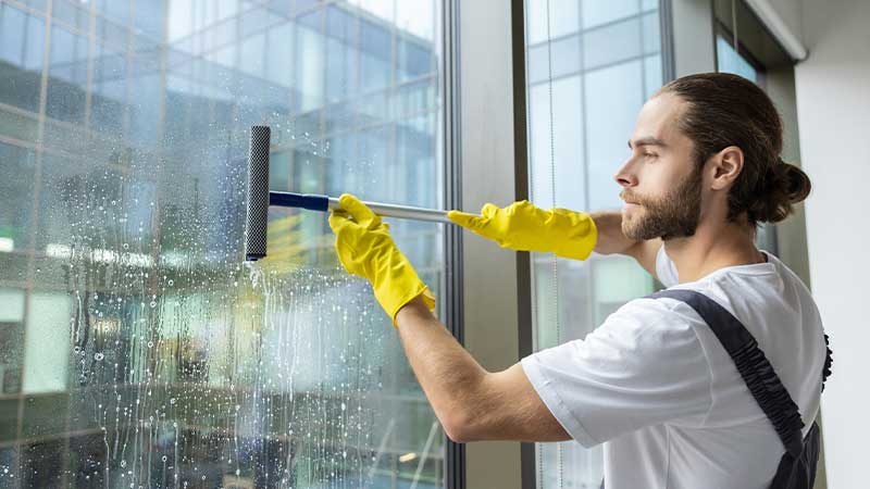 Homem com luvas amarelas e um rolo de limpeza, limpa um vidro de janela
